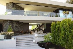 Terrace with outdoor furniture and decorative white balls on steps below upper storey of contemporary house with glass balcony balustrade