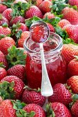 A jar of strawberry jam surrounded by fresh strawberries