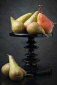 Several pears on and next to a cake stand