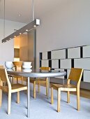 Holzstühle an Tisch mit geschwungener Tischplatte unter Designer Stab Pendelleuchte, an Wand zeitgenössisches Regal mit weissen, schiebbaren Fronten