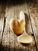 A heart-shaped potato and a wooden spoon on a wooden surface