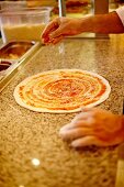 Pizza base being sprinkled with cheese