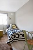 Metal standard lamp over bed with textiles in graphic patterns and olive green, vintage metal chair in foreground chair