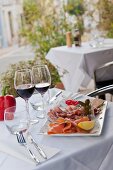 Antipasti platter and glasses of red wine on a restaurant table outdoors (Italy)