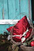 Rotes Seidenkissen mit nostalgischer Weihnachtsdeko vor türkisfarbenem Hütten-Fensterladen