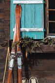 Vintage Skier an Hüttenwand und türkisfarbenem Fensterladen gelehnt