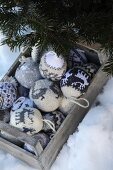 Grau-weiße Strickkugeln mit Norwegermuster in verwitterter Holzkiste und Tannenzweig im Schnee