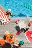 Relaxen am Pool - Orangefarbene Terrassenmöbel und weisser Metallgeflecht-Stuhl auf sonnenbeschienener Holzterrasse am Pool