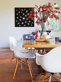 White shell chairs with wooden frames at rustic table, breakfast place settings around huge vase of berries and black and white picture in background