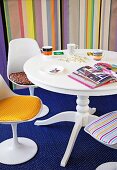 Mustermix - Weisser, runder Tisch, Schalenstühle mit farbigen Polstern auf blauem, gemustertem Teppich, im Hintergrund gestreifte Wandtapete