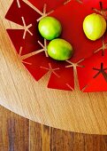 Lemons in red metal dish with perforated pattern on wooden surface