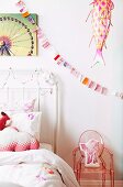 Detail of white metal bed next to child's chair made of transparent pink plastic below bunting and ornamental animal