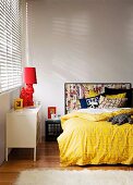 Bett in Jugendzimmer mit selbstgemachtem Kopfteil aus Comicseiten unter Bilderrahmen, selbstgenähten Dekokissen aus alten T-Shirts & Nachttischleuchte aus bemaltem Gartenzwerg