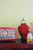 Radio im Fiftiesstil neben Laterne mit schwarzem Metallgestell und rotem Papier vor pastell grüner Wand
