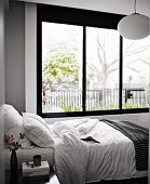 Einzelbett vor breiter Fensterfront im Schlafzimmer in grau-weissen Tönen