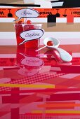 Cocktail cherries in beakers with name tags and white china spoon on red, reflective glass surface