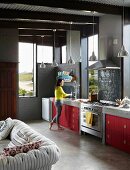 Offene Küche eines Architektenhauses mit roten Küchenfronten, Estrichboden und sichtbaren Deckenbalken