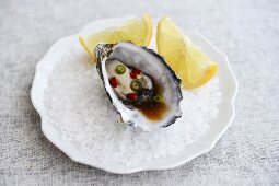 A fresh oyster with Thai chilli dressing and lemon wedges on rock salt