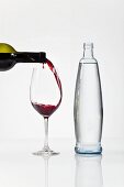 Red wine being poured into a glass, next to a bottle of water