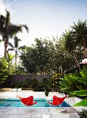 Pool with two red butterfly chairs behind glass balustrade