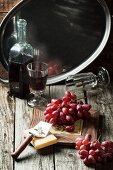 Bunch of red grapes with cheese and vintage bottle of red wine on old wooden table
