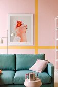 Petrol-blue sofa below picture of bird on pink wall with yellow stripes