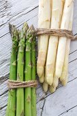 Green and white asparagus, tied in bundles, on a wooden surface