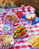 A garden table laid with grilled corn on the cob, salad, crisps and apple pie