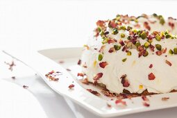 A Bundt cake with white icing, pistachios and rose petals