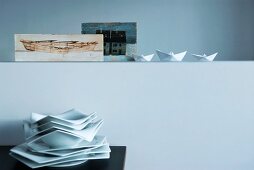 Stack of polygonal plates below paper boats and Nordic painting arranged on half-height wall