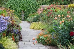 Multicoloured flowers lining paved path in English garden with brick wall