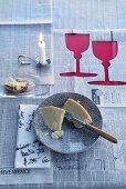 Newspaper tablecloth with cut-out silhouettes of wine glasses, napkin scribbled with writing and spoon-shaped candlestick