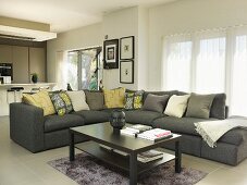 Coffee table in front of corner sofa with scatter cushions in open-plan interior