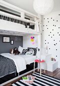 White wooden bunk beds with black and white bed linen and striped rug in children's bedroom