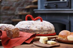 Selbst gehäkelter Filz-Deckel als Brotaufbewahrung, frisches Brot und Butter auf Holztisch