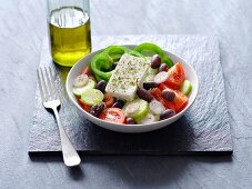 A Greek salad next to a bottle of olive oil