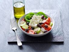 Griechischer Salat, daneben eine Flasche mit Olivenöl