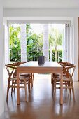 Schlichter eleganter Holztisch mit Hans Wegner Holzstühlen und Gartenblick mit Palmen