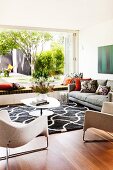 Stylish living room with designer furniture, graphic black and white rug and open terrace window with view into summer garden