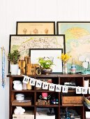 Framed pictures stood on top of antique wooden shelving unit holding various crockery decorated with garland of letters