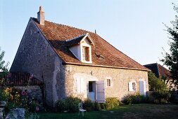 Old, French farm house with white window shutters in simple, one-storey stone facade