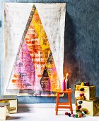 Artistic wall hanging of stylised Christmas tree on grey wall above presents wrapped in gold paper and lit candles