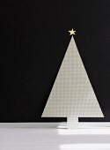 Minimalist, stylised Christmas tree cut from perforated sheet metal with gold star on top against black wall