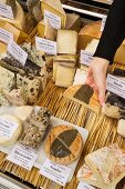 A woman taking a piece of cheese from a cheese display