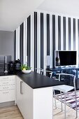 Open-plan kitchen with black worksurface on breakfast bar and bar stools; TV on sideboard against elegant, black and white striped wallpaper in background