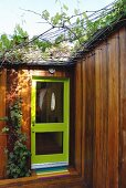 Haustür mit grünem Rahmen und Glasfüllung in modernem begrüntem Holzhaus mit Rankhilfe