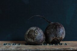 Two beetroots on a wooden crate against a dark background