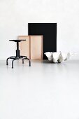 Still-life arrangement of swivel stool, black panel, giant clam shell and empty drawer against patinated wall