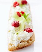 Slice of bread topped with cream cheese, cucumber and raspberries
