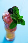 A cocktail with berries and a sprig of mint